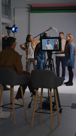 Vertical-Video-Of-Female-Assistant-Using-Clapperboard-As-Actors-Shoot-Movie-Or-Video-In-Studio-With-Film-Crew-And-Director-Shot-In-Real-Time-1